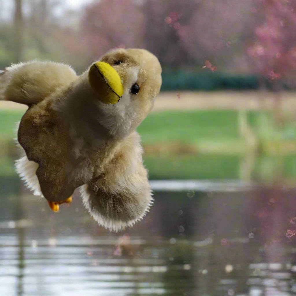 Plush toy duck flying above water with a blurred natural background